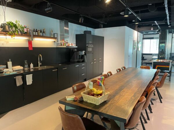 Moderne kantoorkeuken aan de De Cuserstraat met een lange houten eettafel, zwarte kasten en een goed gevulde fruitmand.